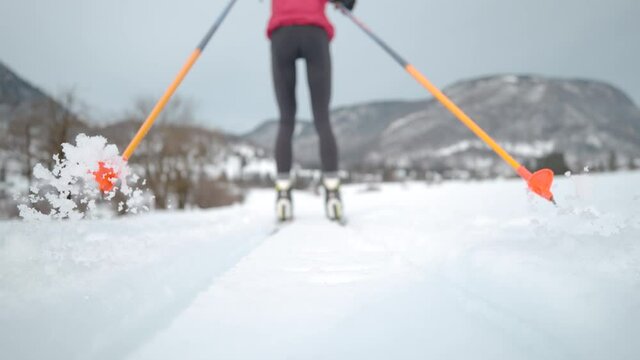 SLOW MOTION, LOW ANGLE, CLOSE UP, DOF: Unrecognizable female athlete trains nordic skiing. Woman nordic skiing pushes off her poles and skis along two tracks running around the Olympic training center