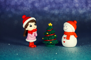 Small table figurines of a girl, a snowman and a Christmas tree on a shiny paper background. New Year photo postcard