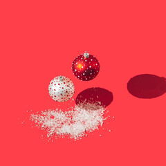 A red Christmas decoration bauble with white dots and a white with red dots falling on a bright red background with artificial snow. Vibrant concept for Christmas or New Year celebration web banner 