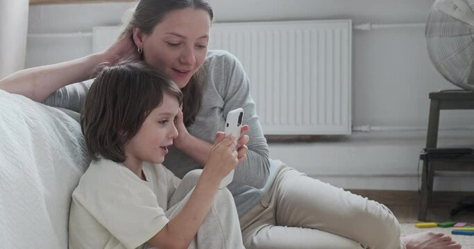 Shocked woman babysitter and smiling kid boy use smartphone together playing online video games weekend activity. Happy male child having internet digital entertainment on mobile phone enjoy childhood
