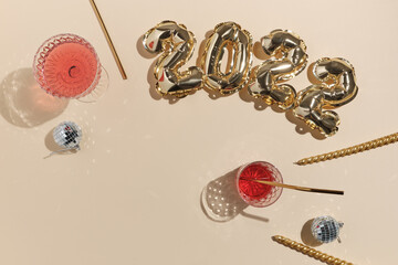 beige festive background for new year or christmas with pink drinks wine, juice, punch, champagne and foil gold balloons in the shape of 2022