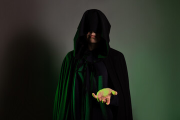 A mystical character in a black hoodie stretches out his hand to you. Witch in a black hood on her...
