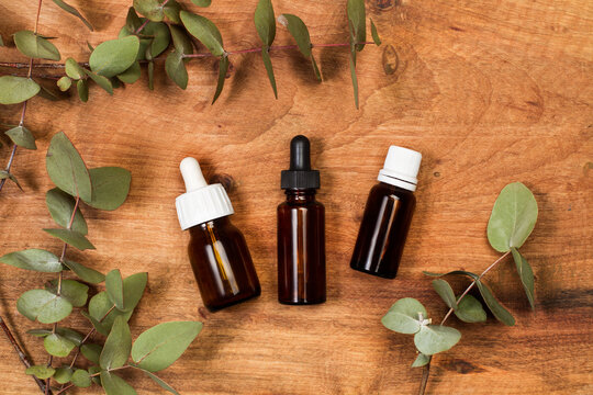 Tres botellas de cristal peque&ntilde;as con gotero junto a ramas y hojas de eucaliptus sobre un fondo de madera r&uacute;stico. Vista superior. Copy space