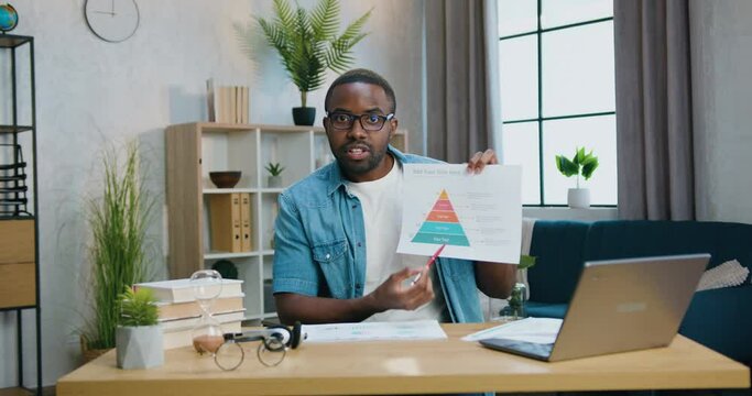 Remote work concept where likable confident purposeful qualified bearded african american worker explaining graph into camera from home office
