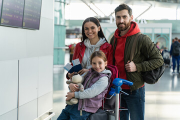 Happy family posing to the camera with suitcases in the airport. Mother, father and daughter looking at the camera with pleasure smiles