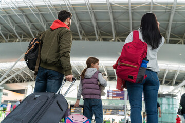 Back view of the family of tourists carrying suitcases and going though the airport after the flight. Traveling and trip concept