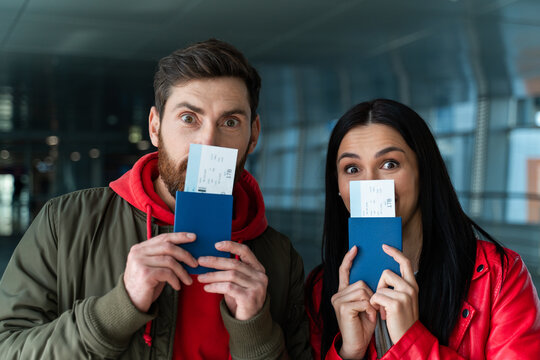 Portrait view of the travel couple hiding their faces behind the passports and tickets during standing at the airport hall before their journey. Stock photo