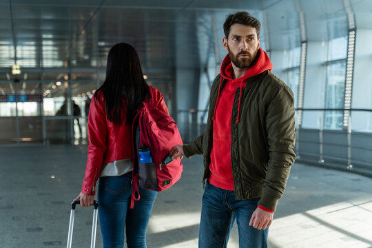 Full length of the bearded thief stealing something from the backpack of brunette woman in the lobby of airport. Criminal concept