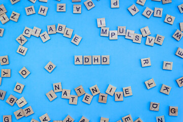 Wooden blocks with letters ADHD and chaotic words on a blue background. Minimal concept of attention deficit hyperactivity syndrome. Selective focus