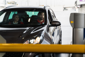 Bearded man sitting at the drivers place with his wife in front of the barrier and waiting while it raise. Drivers and cars concept