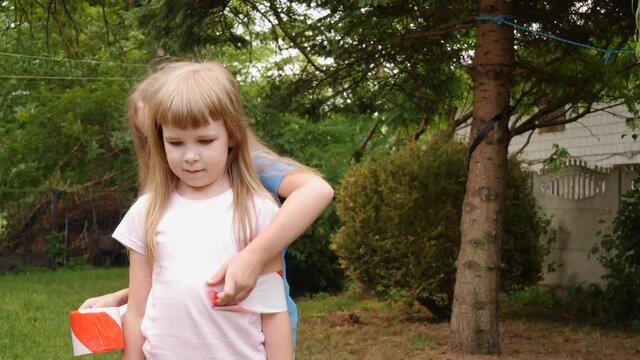 Young girl, little elementary school age child being wrapped in red white safety hazard tape by her sister. Striped security tape wrapping concept, children, funny quirky lifestyle shot fooling around