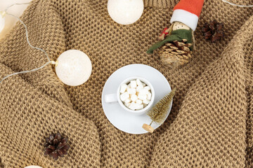 A cup of coffee, Brown knitted sweater and garlands, led lights. Women fashion winter clothes and accessories. New year and Christmas celebration mockup. Christmas still life
