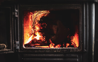 Fire burning glowing in rustic wood burning cast iron stove, log burner for heating or fireplace
