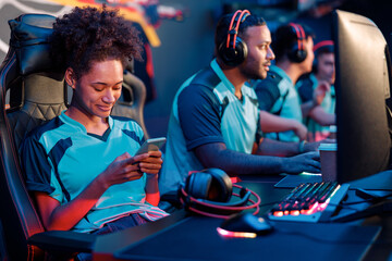 Cute female cybersport gamer sitting in gaming chair and playing mobile game on cellphone in computer club