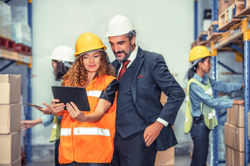 Manager using tablet with supervisor using tablet showing order to manager with blurred workers checking stock in the warehouse  