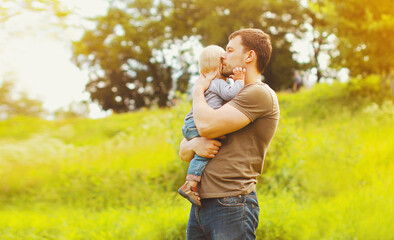 Portrait of pensive young father holding his son child looking away in summer park