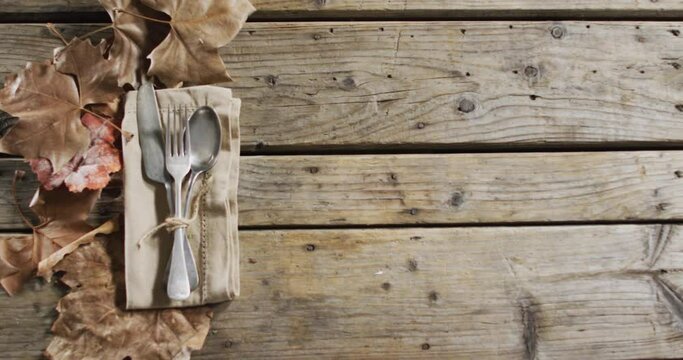 Close up view of cutlery set over a napkin and autumn leaves with copy space on wooden surface
