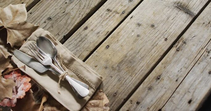 Close up view of cutlery set over a napkin and autumn leaves with copy space on wooden surface