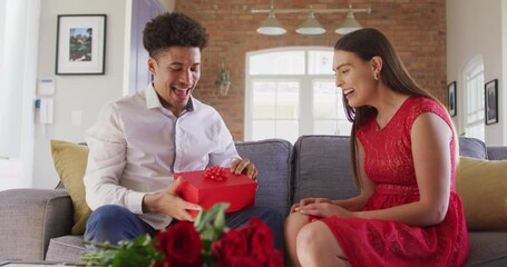 Happy biracial couple celebrating valentine's day giving presents at home - Powered by Adobe