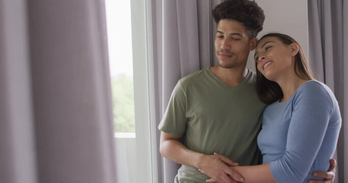 Happy biracial couple embracing and looking throught window together