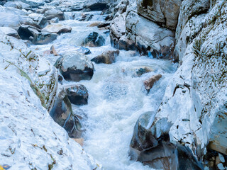 A turbulent foamy river flows over large rocks in a rocky gorge. Canyon white rocks