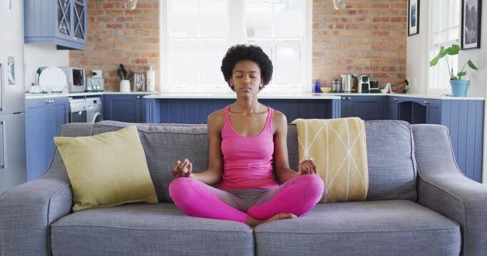 Relaxed african american teenage girl sitting on sofa doing yoga and meditating