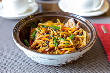 Noodles with beef and vegetables in teriyaki sauce. Beans, sesame seeds. Noodles, a ready-made dish in a restaurant. Grey tablecloth. Lunch at the restaurant
