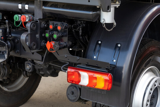 Detail of the rear of a new utility truck. Taillights, electrical connectors, plastic mudguards, wheels and rims. Red brake lights and orange turn signals. Road safety