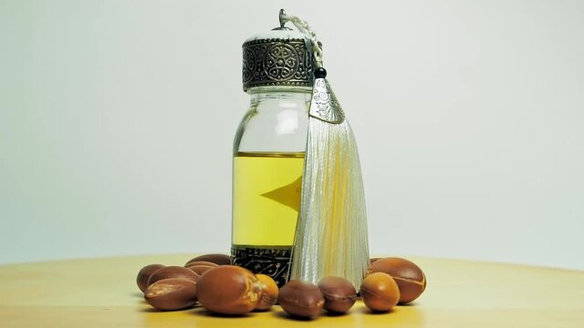 Argan oil in a oriental glass and metal bottle and argan nuts motion on wooden table and white background.