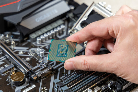 A technician holds the CPU Intel i7-9700K against the background of the motherboard Gigabyte. Installing a CPU into socket on a motherboard. PC assembly concept. Russia, Moscow - May 16, 2020