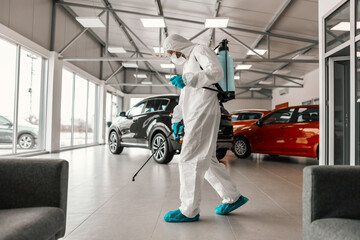 Destroying bacteria and viruses on an electric treadmill in closed modern showroom space. A man in a protective uniform and a sprayer cleans high-risk areas of infection. Coronavirus, corona, COVID19