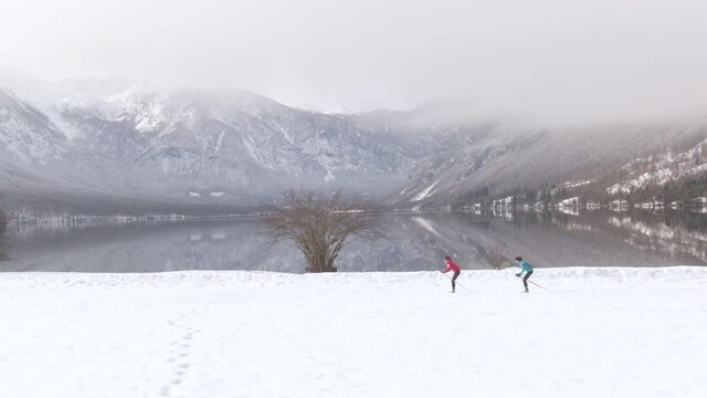 AERIAL: Flying along two female athletes training nordic skiing for the Olympics near lake Bohinj. Professional nordic skiers train at a scenic training center in the picturesque mountains of Slovenia