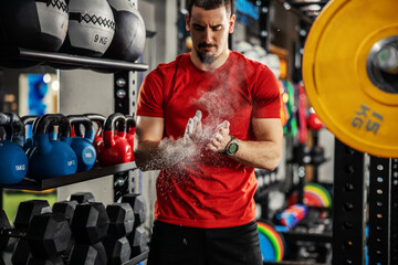 Weightlifter clapping hands and preparing for workout at a gym. Focus on white powder dust. A man...