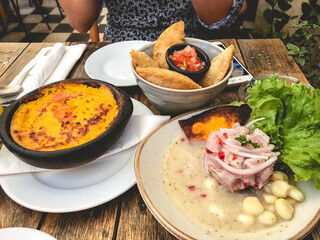 Date table with peruvian 'ceviche' (fresh raw fish cured in fresh citrus juices) in a plate, 'pastel de choclo' (corn cake) and 'empanadas' (fried turnover of pastry and filling)