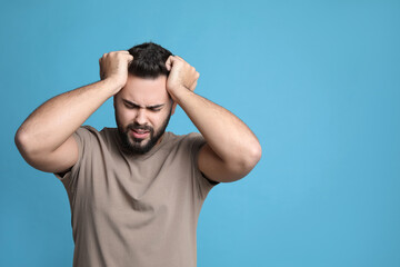 Young man suffering from headache on light blue background, space for text