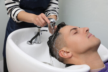 Obraz na płótnie Canvas Professional hairdresser washing client's hair at sink indoors, closeup