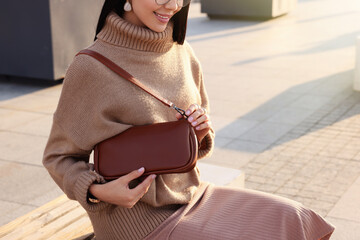 Fashionable young woman with stylish bag on bench outdoors, closeup