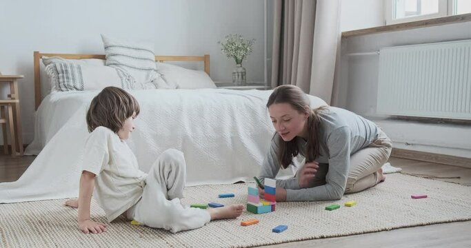 Confident family mom and son building multicolored bricks playing together enjoying weekend at home. Smiling kid boy neatly use constructor block cubes with mother having happy childhood motherhood