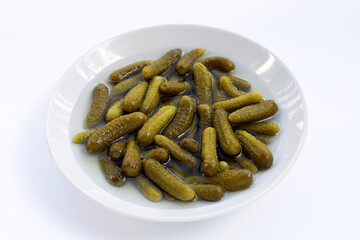 Pickled gherkins or cucumbers in bowl on white background.