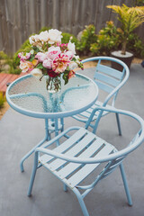 bunch of rose flowers in vase on top of outdoor table in sunny backyard
