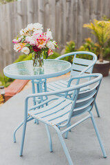 bunch of rose flowers in vase on top of outdoor table in sunny backyard