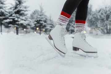 Figure skating woman skating on ice at outside rink during snowfall wearing female white leather boots. Family outdoor activity winter sport