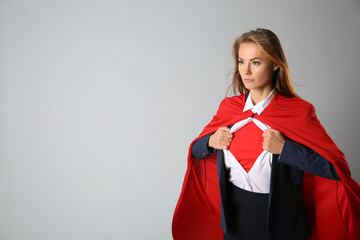 Confident businesswoman wearing superhero costume under suit on light grey background. Space for...