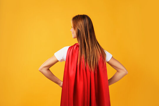 Woman wearing superhero cape on yellow background, back view