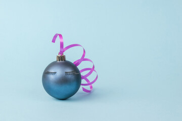Christmas ball with eyelashes and pink ribbon on a blue background. The minimum concept of the New Year.