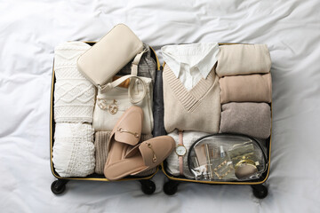 Open suitcase with folded clothes, shoes and accessories on bed, top view