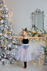 a beautiful delicate ballerina in a fluffy white skirt on the side of a decorated Christmas tree