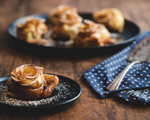 Apple Rose Pastries with single apple rose pastry on a blue plate sprinkled with powdered sugar with blue napkin on wooden table.