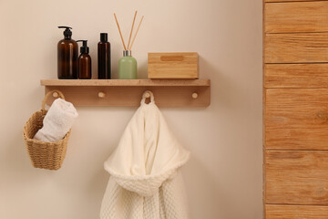 Fototapeta na wymiar Wooden shelf with toiletries, fresh towel and bathrobe on beige wall. Interior element