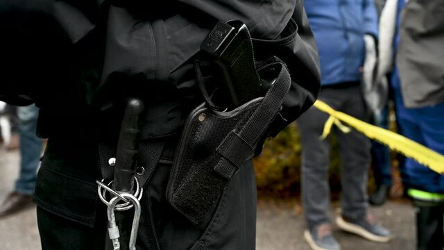 Police officer's belt with a gun and baton tonfa. Policeman standing on the street during protest. Policeman carrying pistol weapon in holster on demonstration.